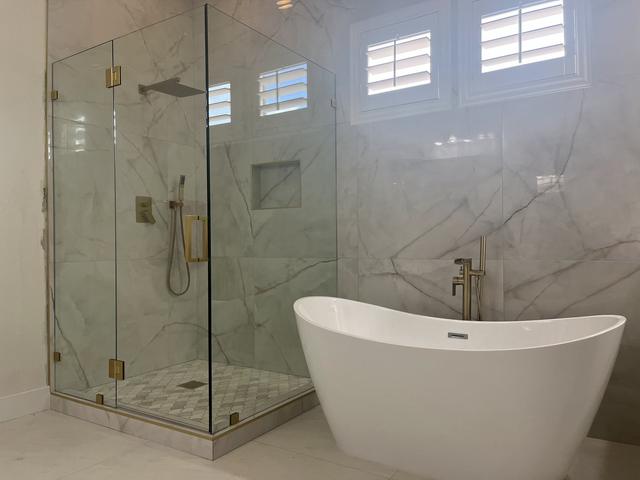 Frameless corner beside a freestanding tub · Satin brass